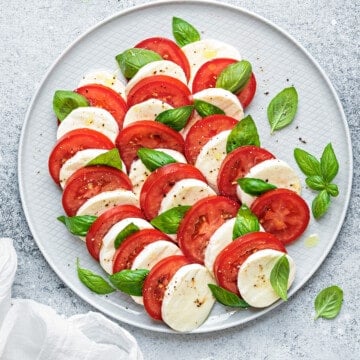 Top down view Caprese salad with tomato, mozzarella, and basil on a light gray plate.