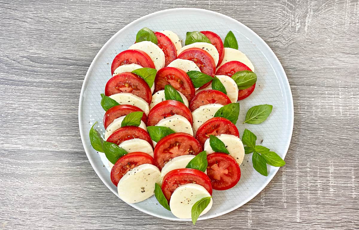 overhead finished shot from Caprese salad recipe, showing layers of tomato and cheese slices with basil.