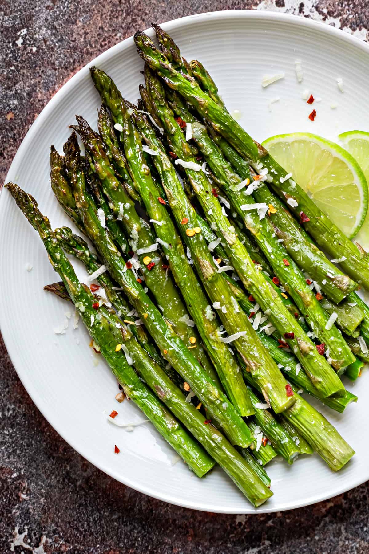 Roasted asparagus on a white plate topped with grated parmesan and lime slices on the side. 