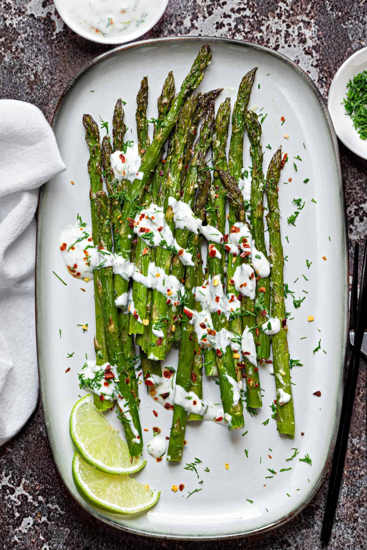 Oven roasted asparagus on a ceramic serving dish, topped with a drizzle of dill sour cream sauce.