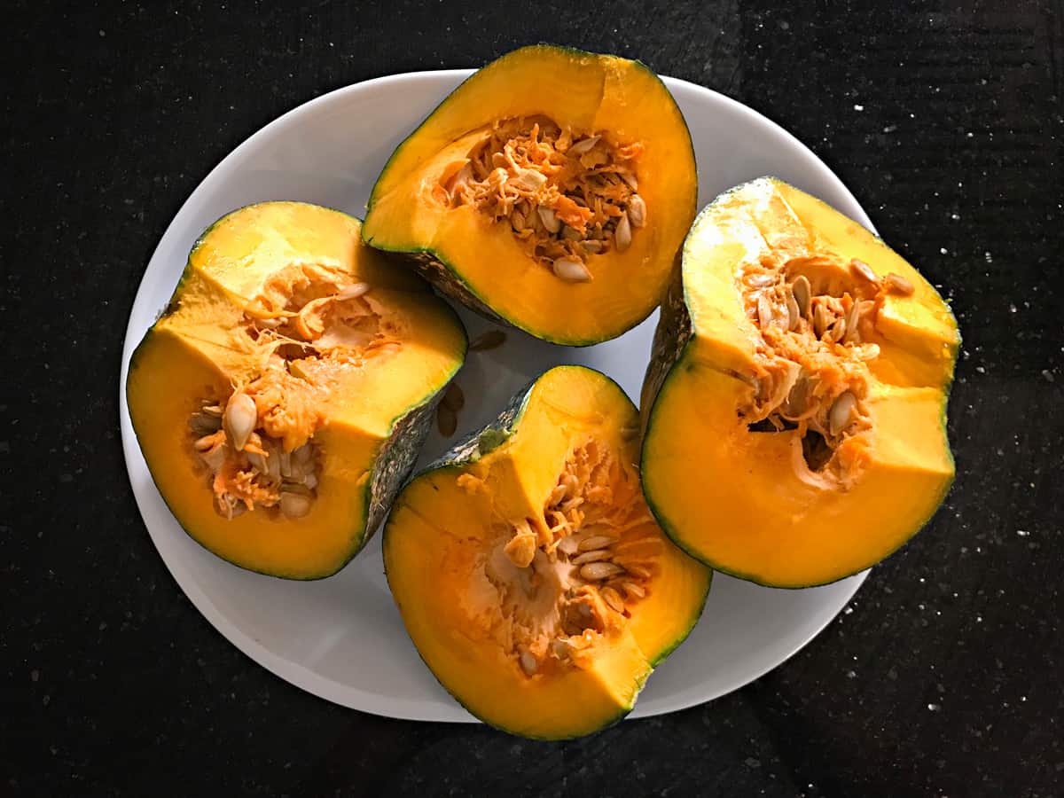 Ripe pumpkin with green skin to make sabzi is cut and placed on a white plate.