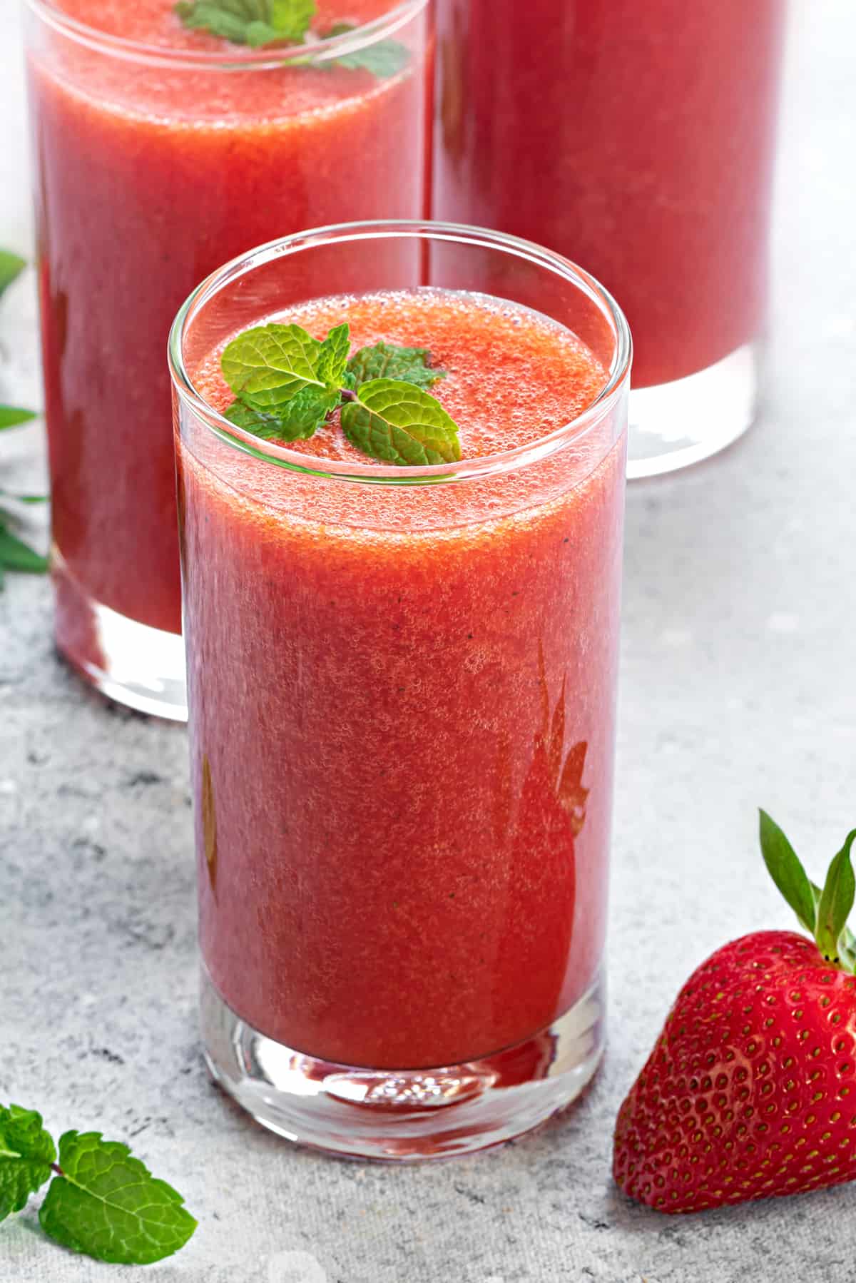 Close-up of fresh strawberry juice in a tall glass garnish with fresh mint.