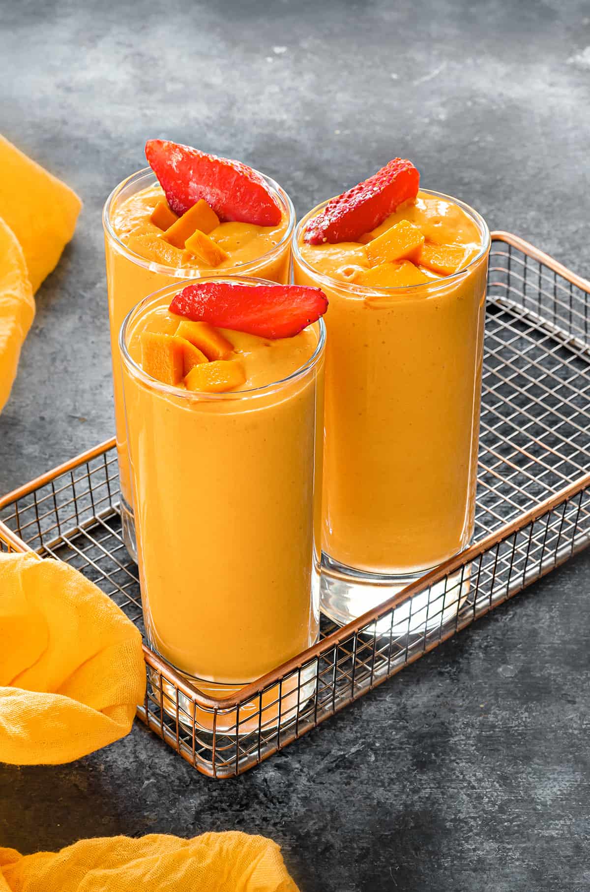 Three tall glasses with strawberry mango banana smoothie in tray placed on a gray table.