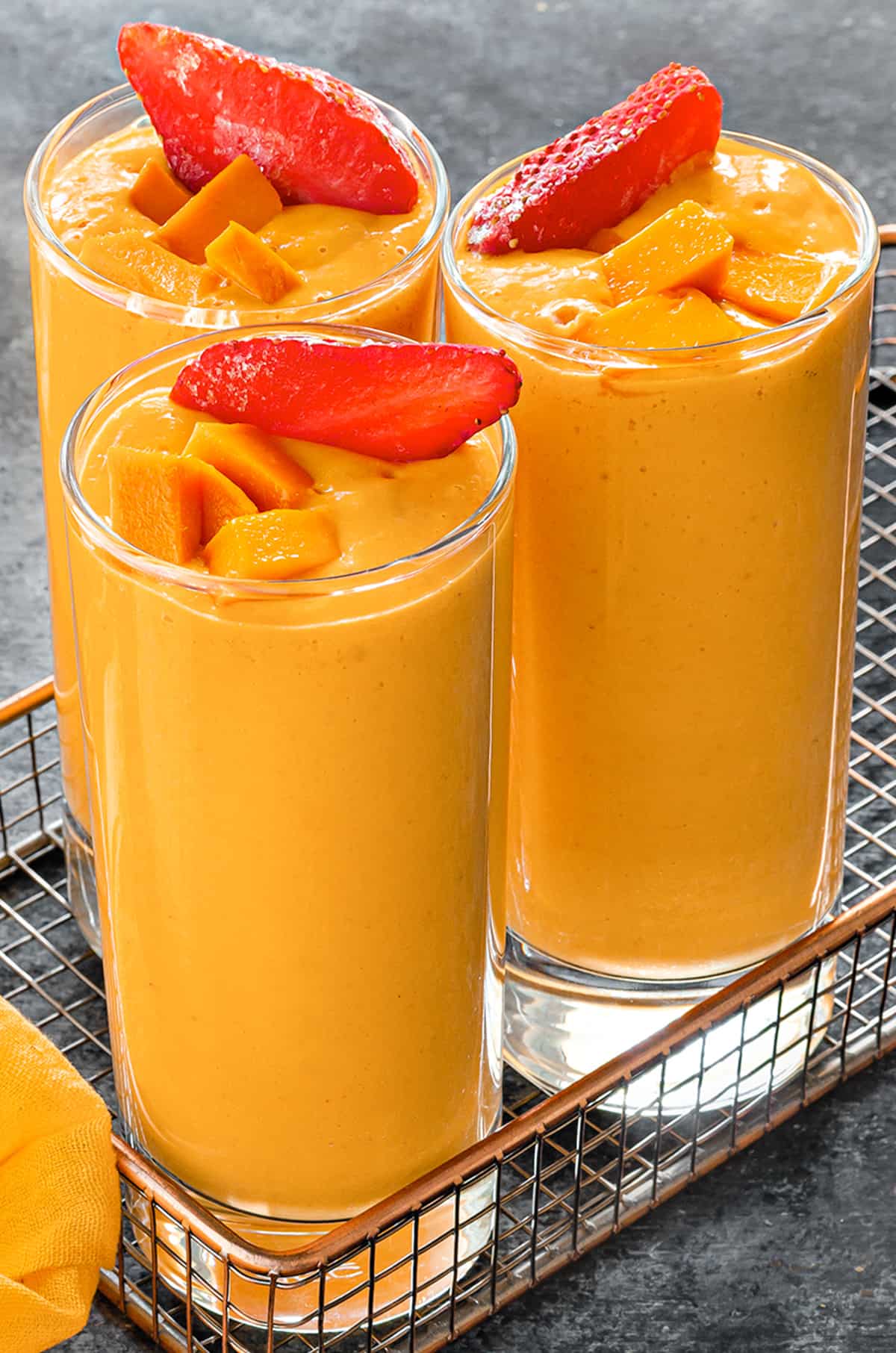 Close view of strawberry mango smoothie served in glasses, garnished with mango cubes and strawberry slices.