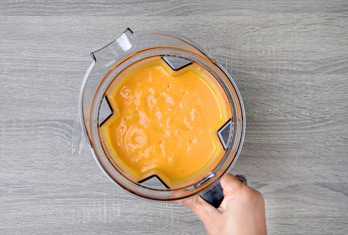 A hand holding a high-speed blender jar with a blended strawberry and mango smoothie.