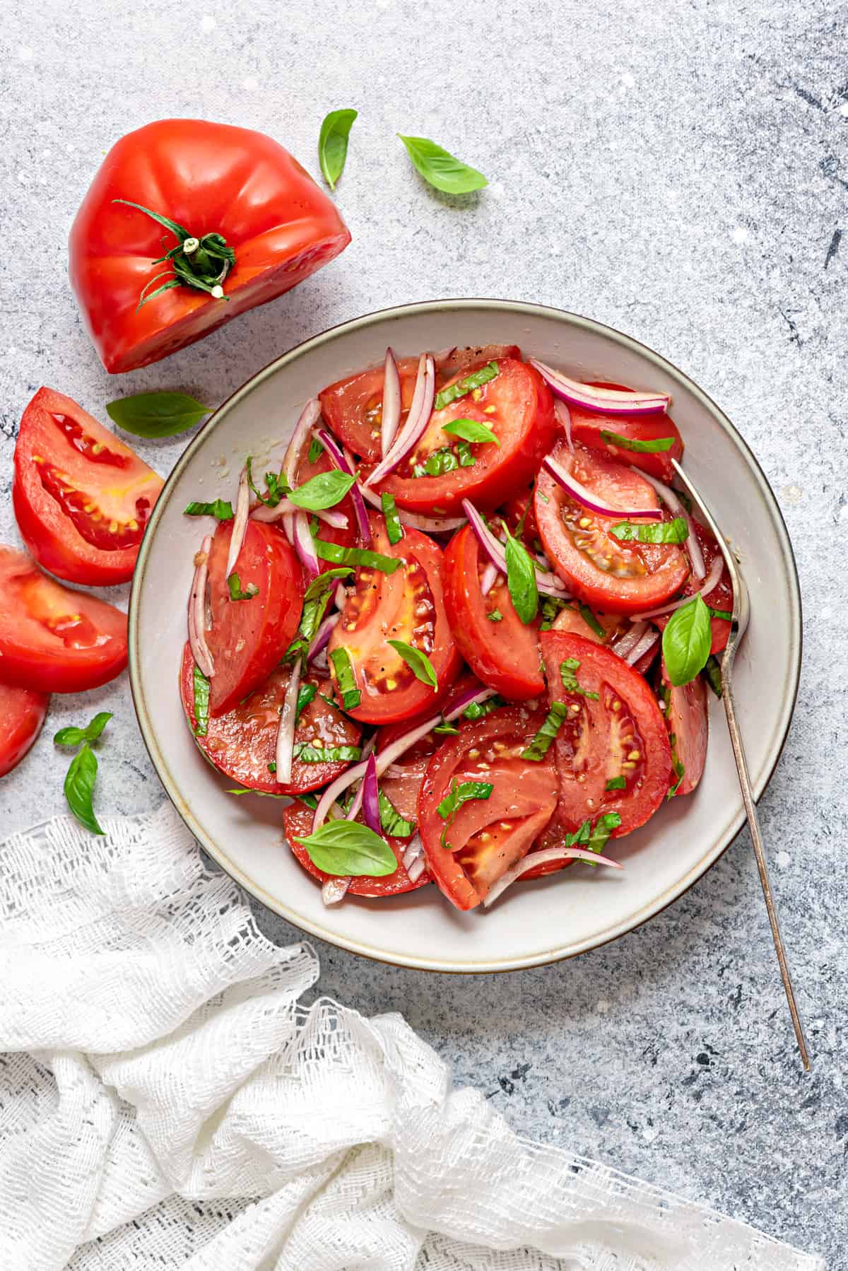 Tomato basil salad served in a grey ceramic plate with a fork, and napkin on side.