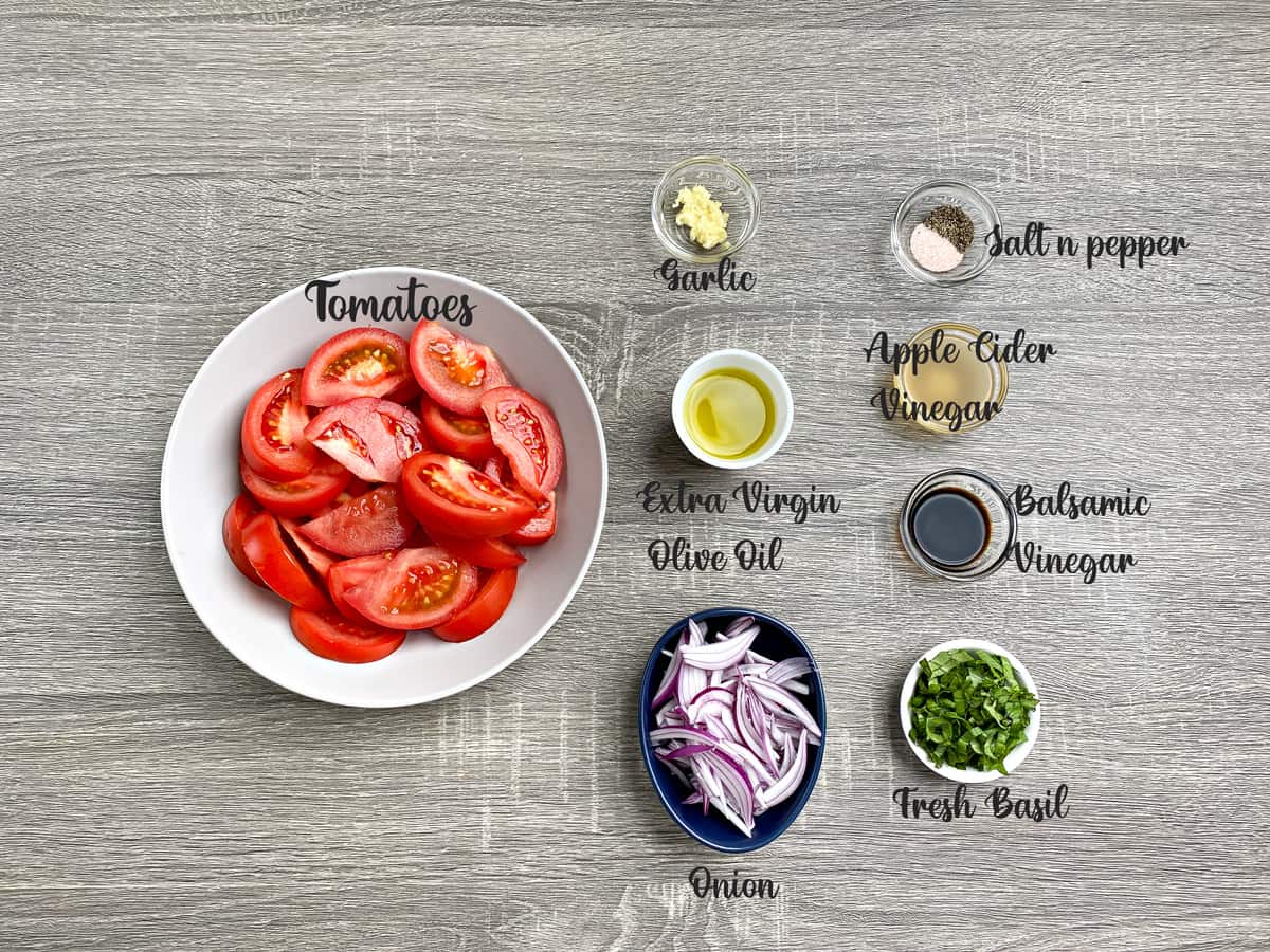 ingredients for tomato basil salad recipe measured in glass bowls placed on a grey table.