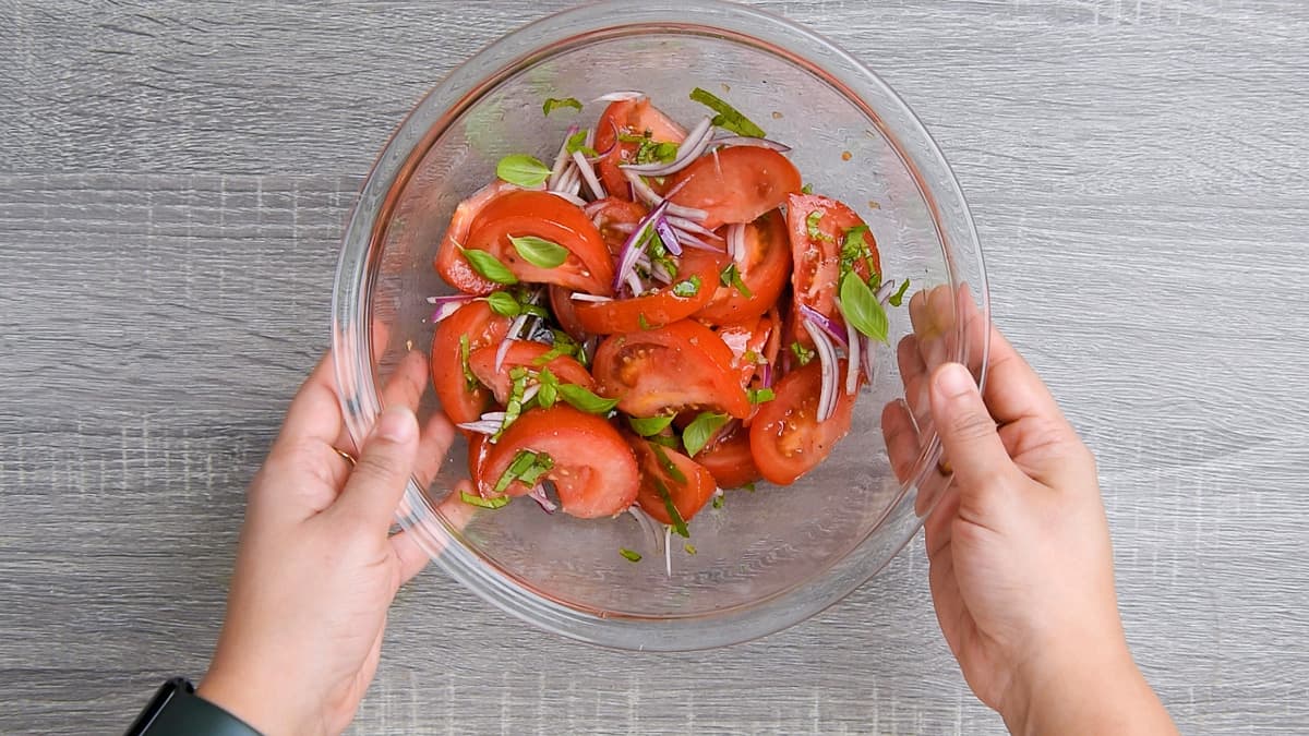 two hands holding tossed basil tomato salad bowl.
