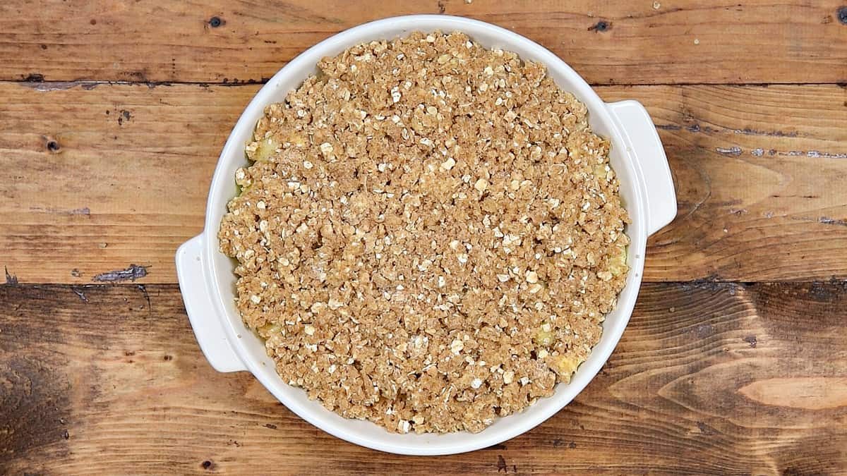 Crumbly oat topping spread evenly on top of spiced apples, crumble is ready to bake.