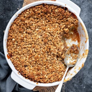Apple crumble with oats topping, a metal spoon and portion removed from the baking dish.