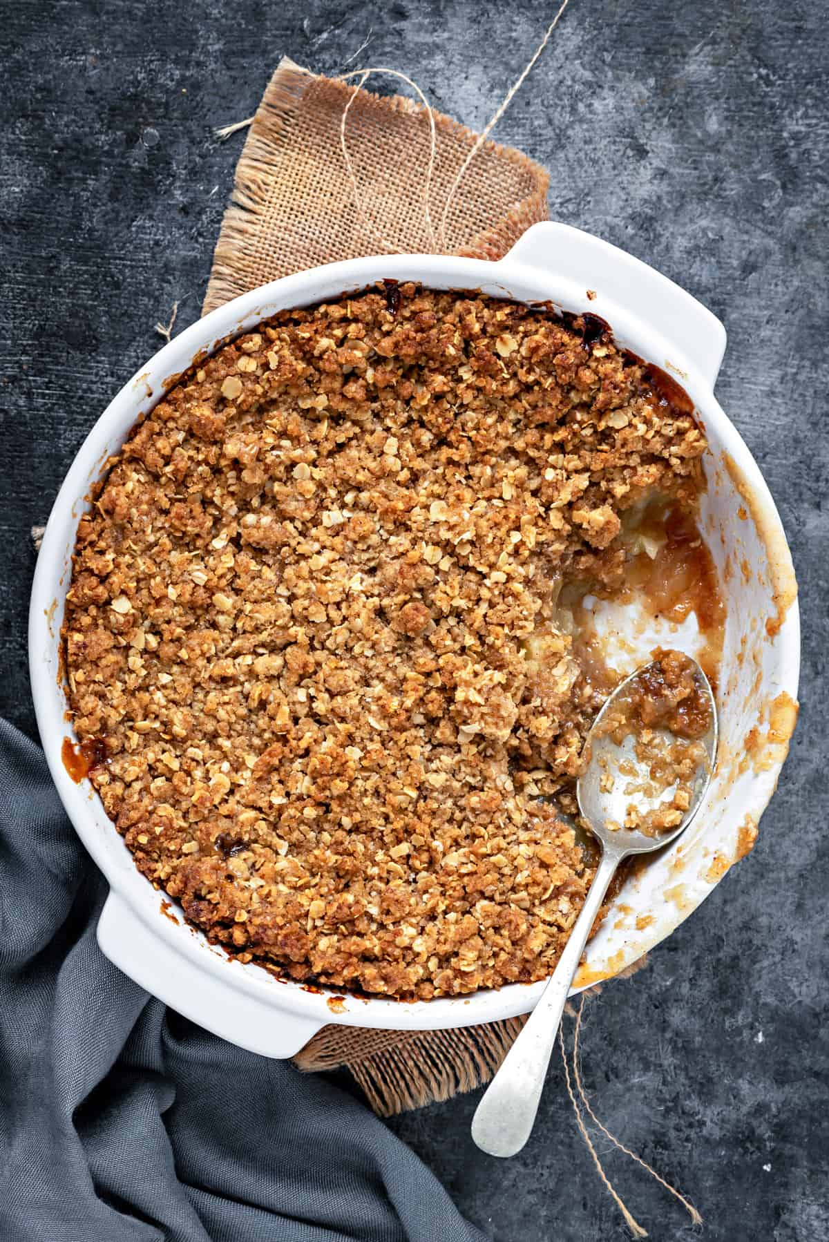 Apple Oats crumble with a metal spoon and portion removed from the baking dish.