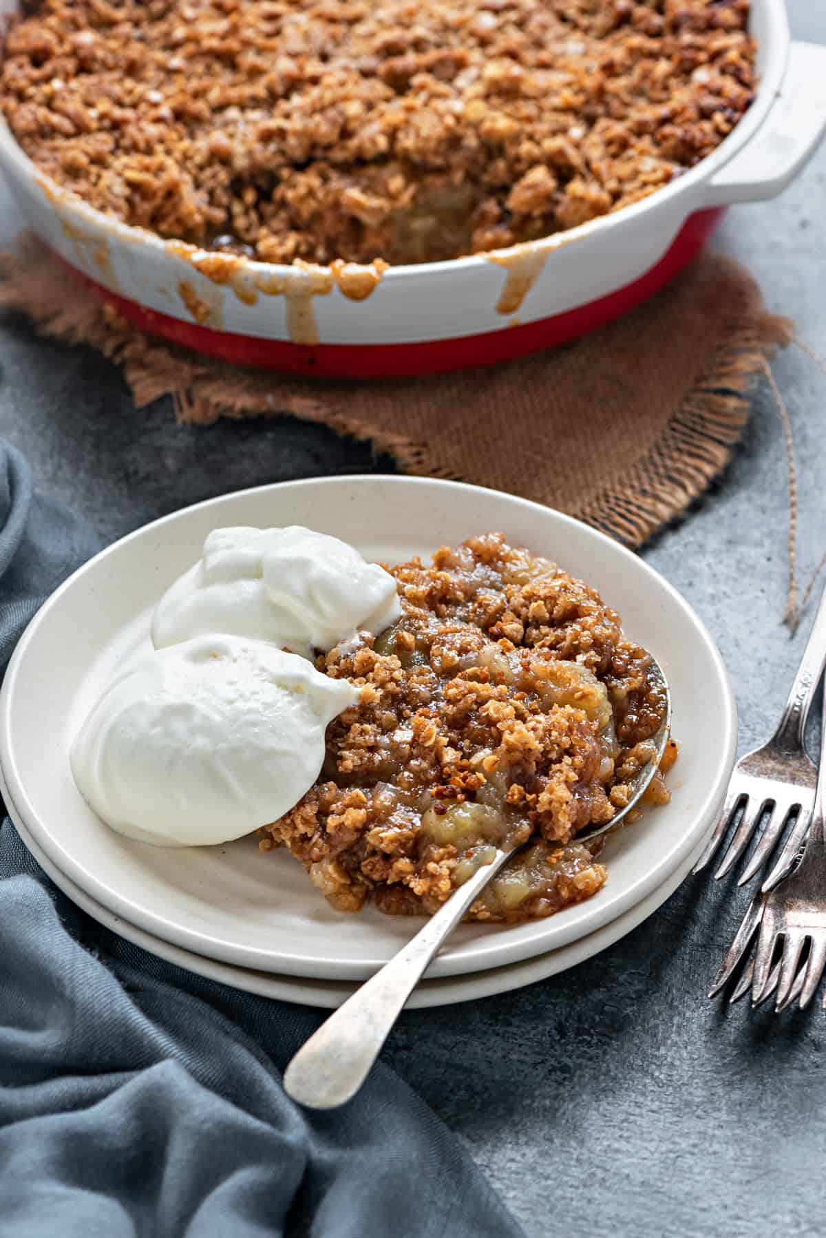 Apple crumble with oats topping on a plate with whipped vanilla cream.