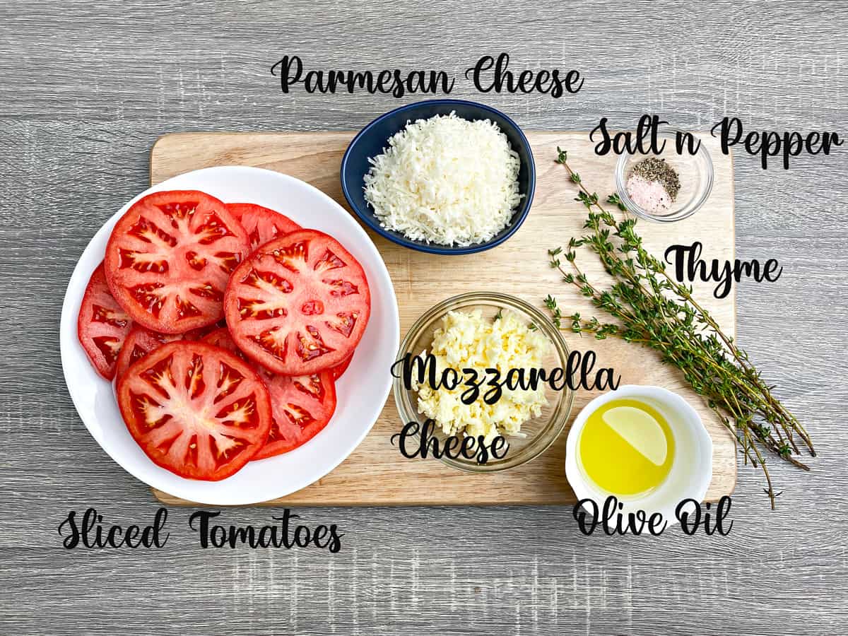 Baked tomato ingredients: sliced tomatoes, parmesan and mozzarella cheese, thyme, olive oil and seasonings in bowls.
