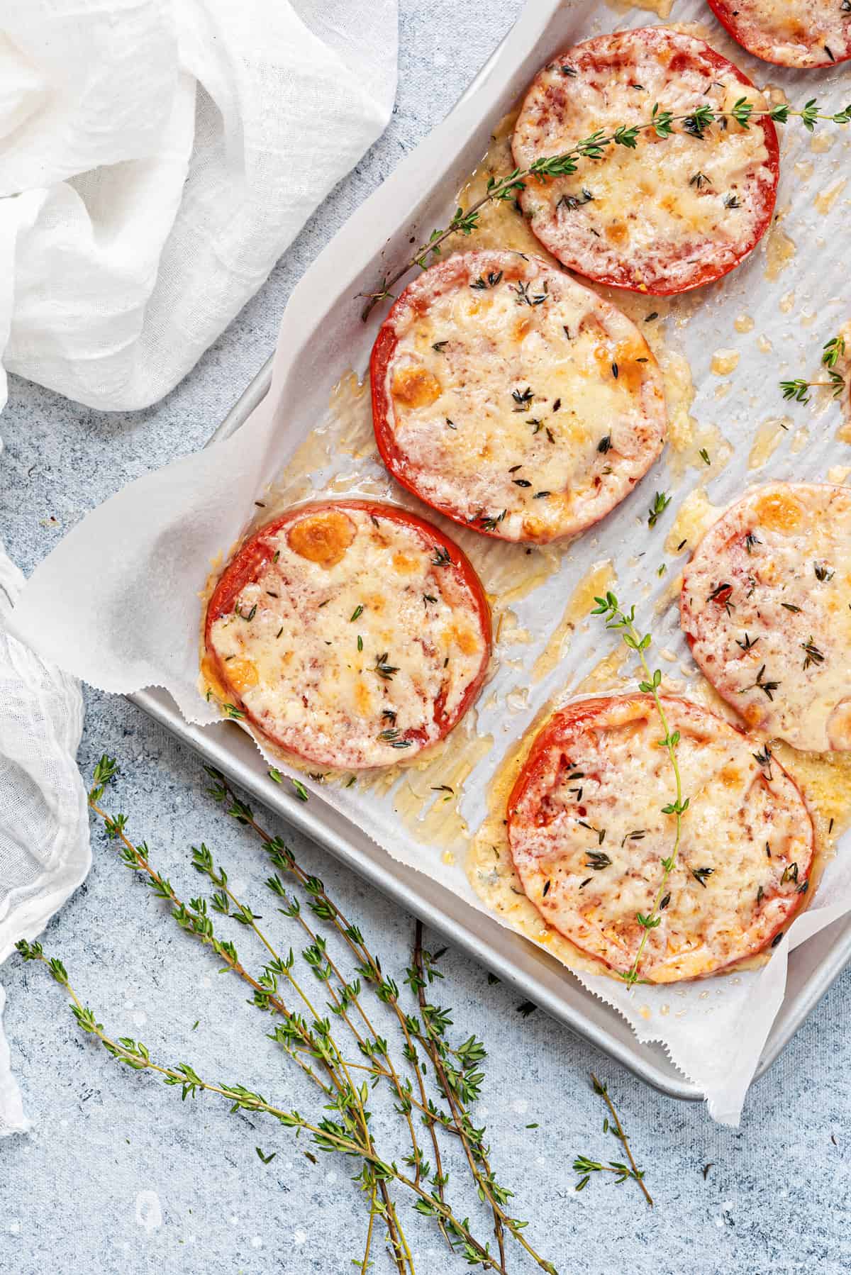 overhead view of freshly baked tomato slices with cheese and thyme on lined sheet pan.