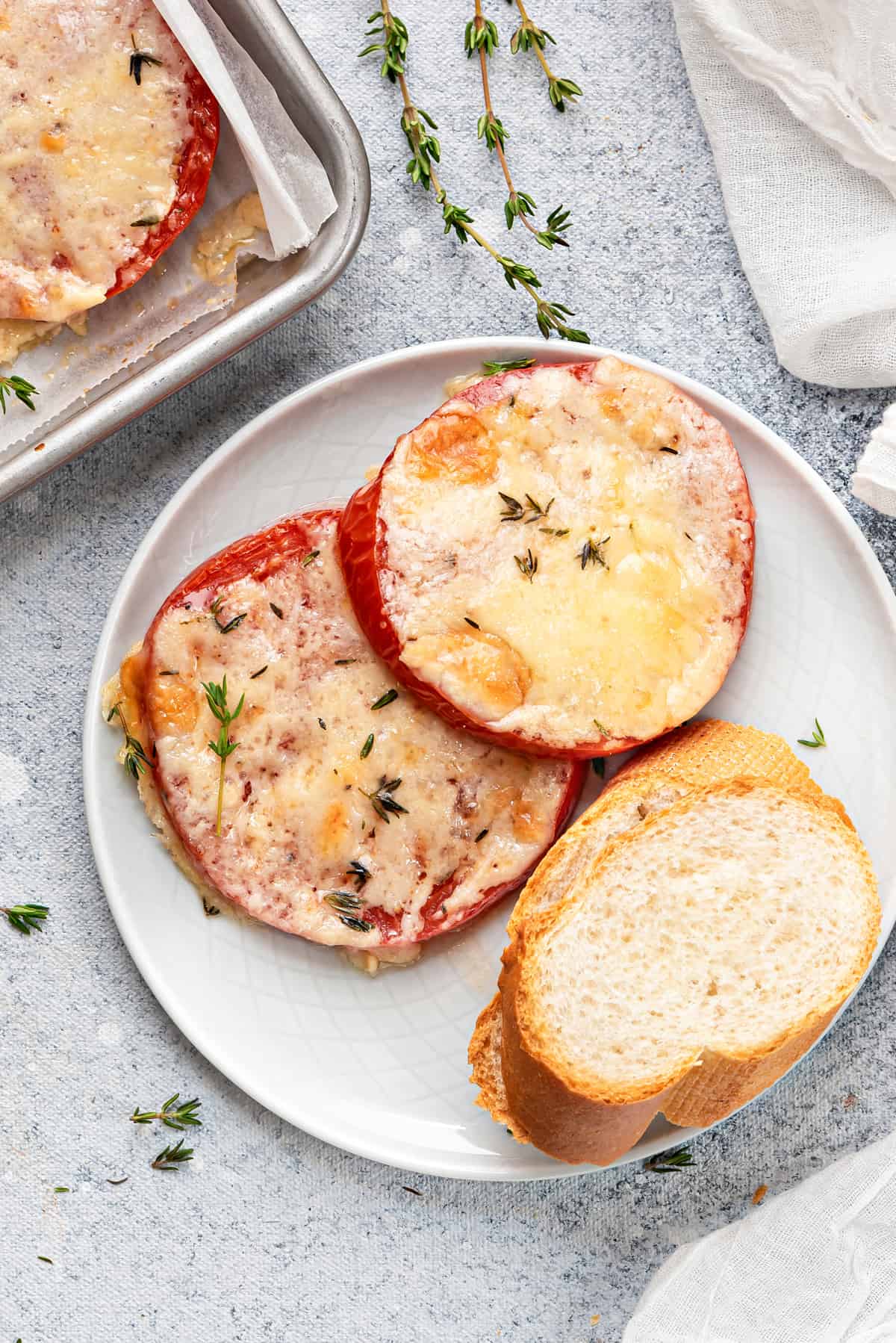 Two slices of cheese baked tomato served on a white plate with bread for breakfast.