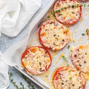 Baked Tomatoes with parmesan and mozzarella cheese on lined baking sheet pan.