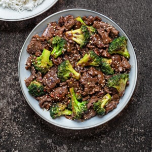 beef and broccoli in a grey bowl topped with red chili flakes and sesame seeds.