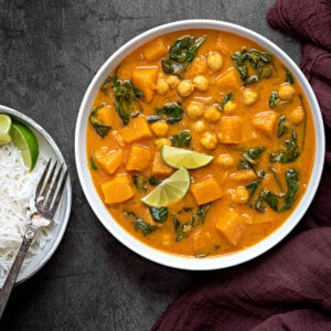 A bowl of butternut squash curry with a plate of rice and a fork on side.