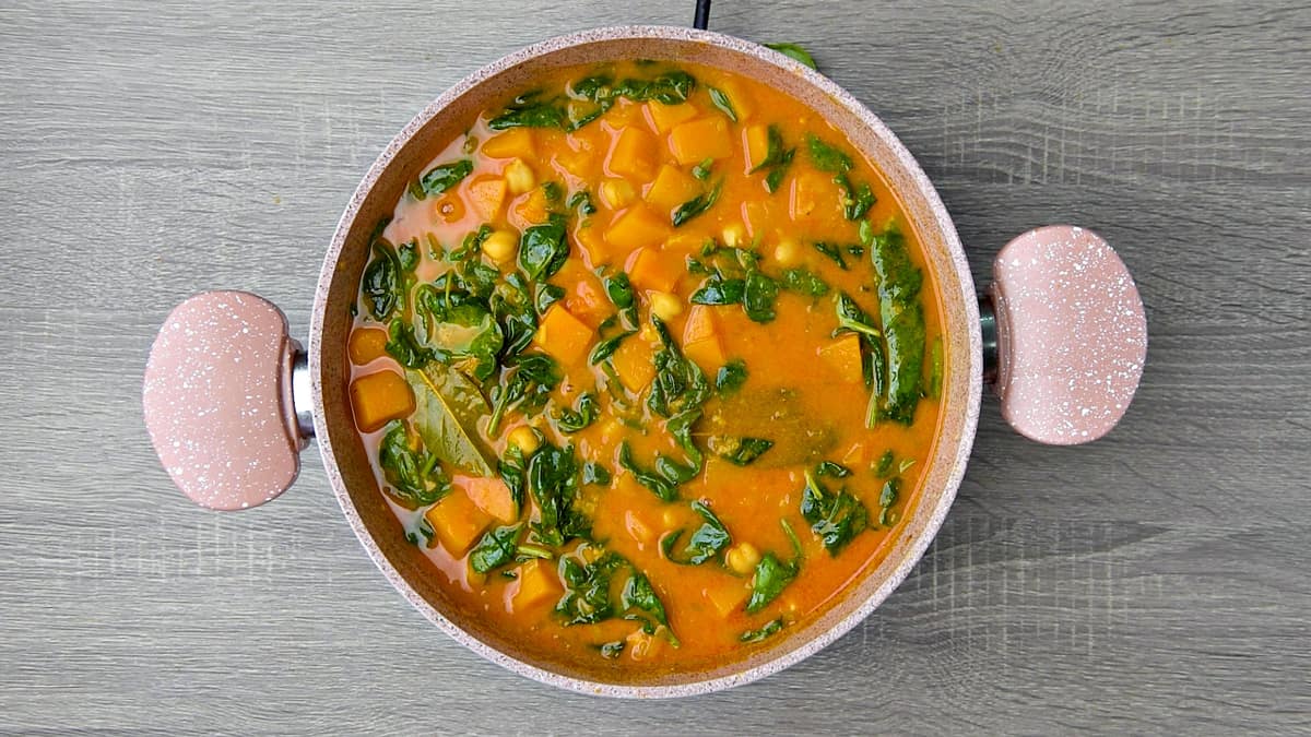Cooked butternut squash curry with chickpeas and spinach in pan ready to serve. 
