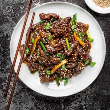 Chinese Beef stir fry in a white pasta bowl with wooden chopsticks on a grey background.