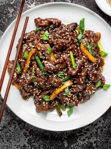 Chinese Beef stir fry in a white pasta bowl with wooden chopsticks on a grey background.