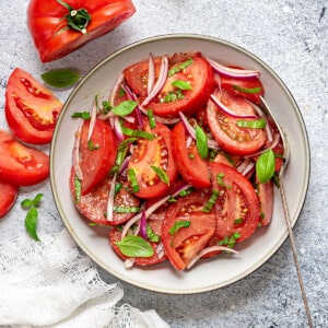 Tomato basil salad served in a grey ceramic plate with a fork, and napkin on side.
