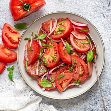 Tomato basil salad served in a grey ceramic plate with a fork, and napkin on side.