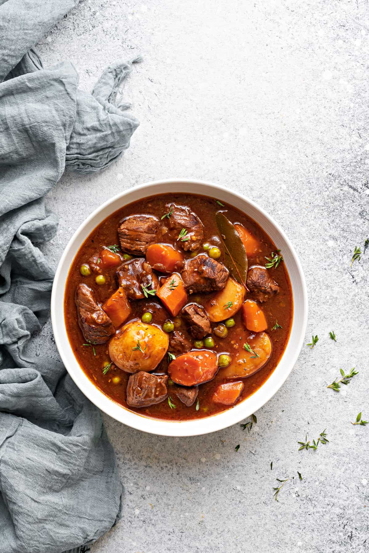 A white bowl of instant pot beef stew meat and gravy with potatoes, carrots and peas.