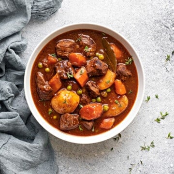 A white bowl of instant pot beef stew meat and gravy with potatoes, carrots and peas.