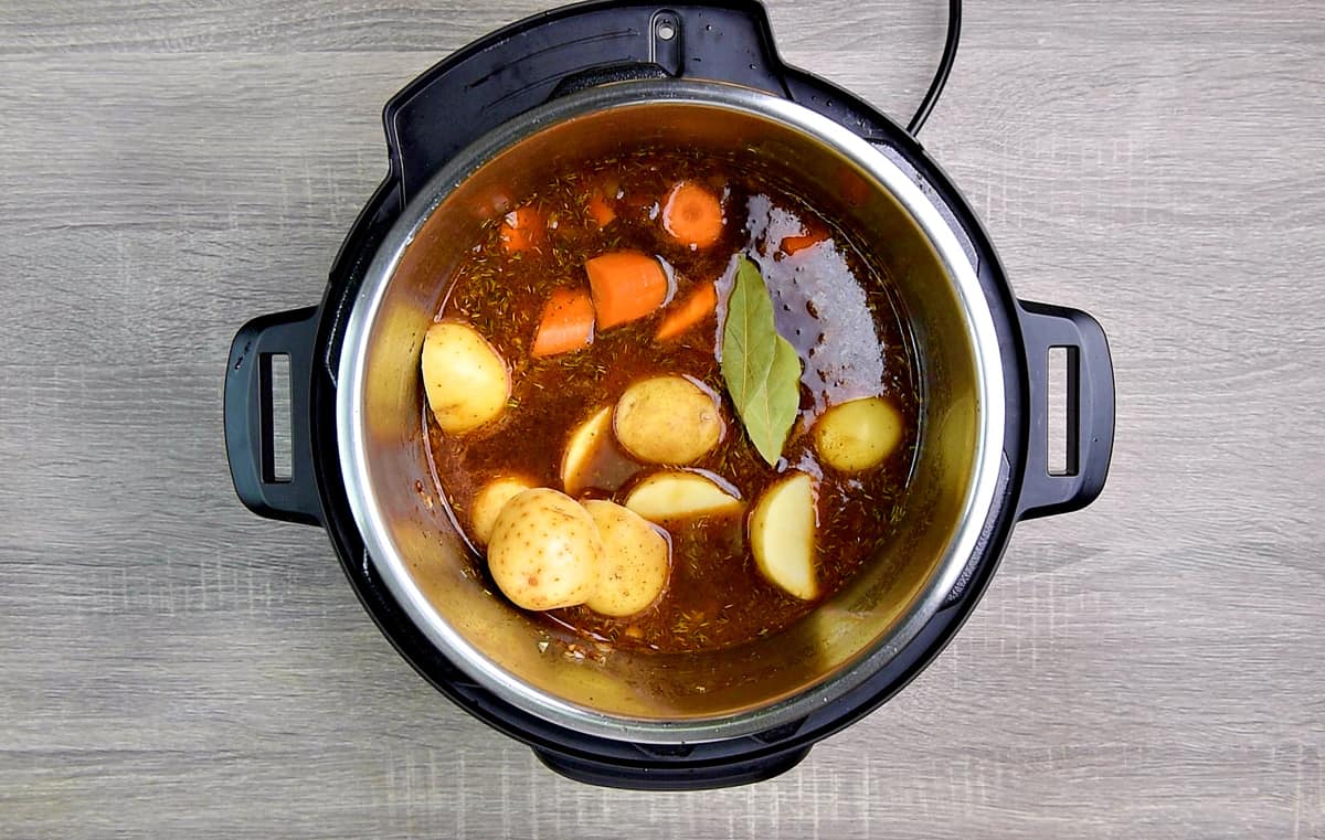 Beef broth, carrots, potatoes and bay leaves added to the instant pot pressure cooker.