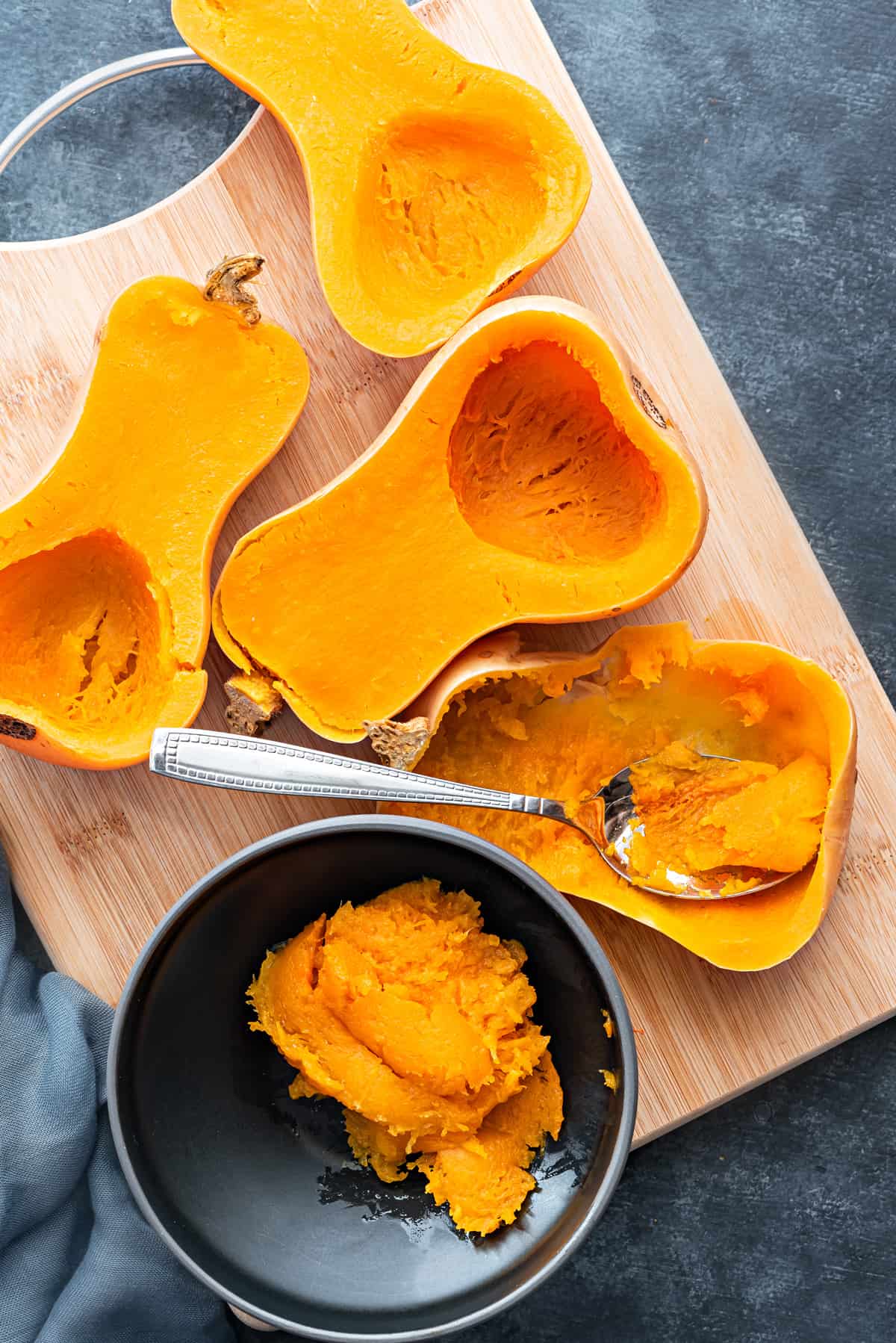 Four pressure cooked butternut squash halves. One halve scooped with a spoon into black bowl.