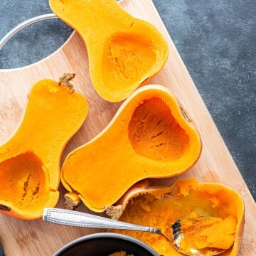 Four instant pot pressure cooked butternut squash halves on wooden board with one halved scooped out.