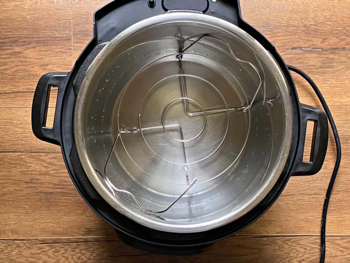 Instant Pot pressure cooker steel insert filled with water and a trivet placed into it.