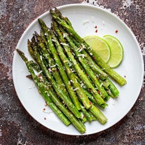 Roasted asparagus on a white plate topped with grated parmesan and lime slices on the side.