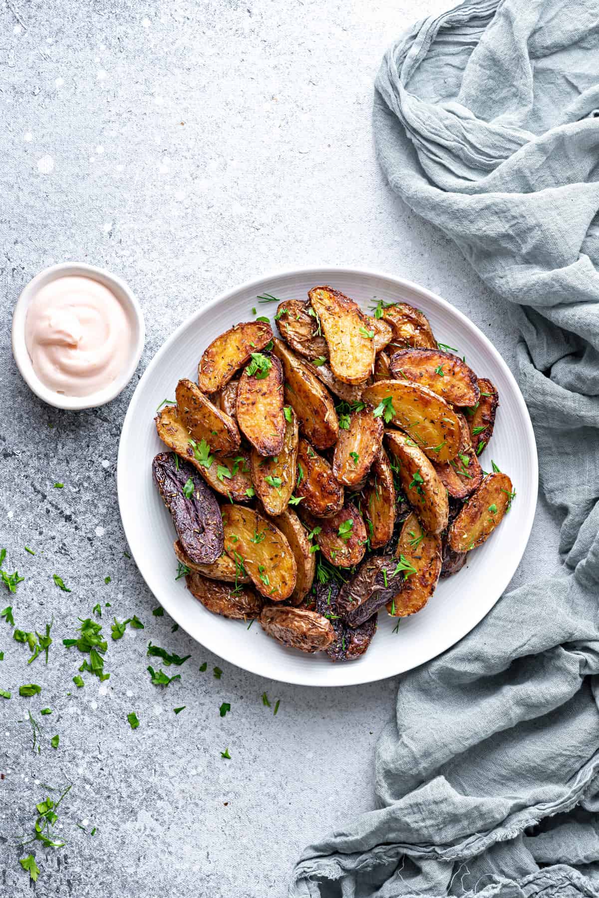 Crisp roasted fingerling potatoes on a plate sprinkled with fresh parsley, dip in bowl on side.