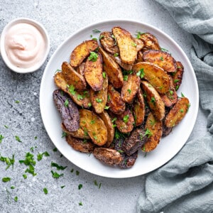 Crisp roasted fingerling potatoes on a white serving plate sprinkled with fresh parsley.