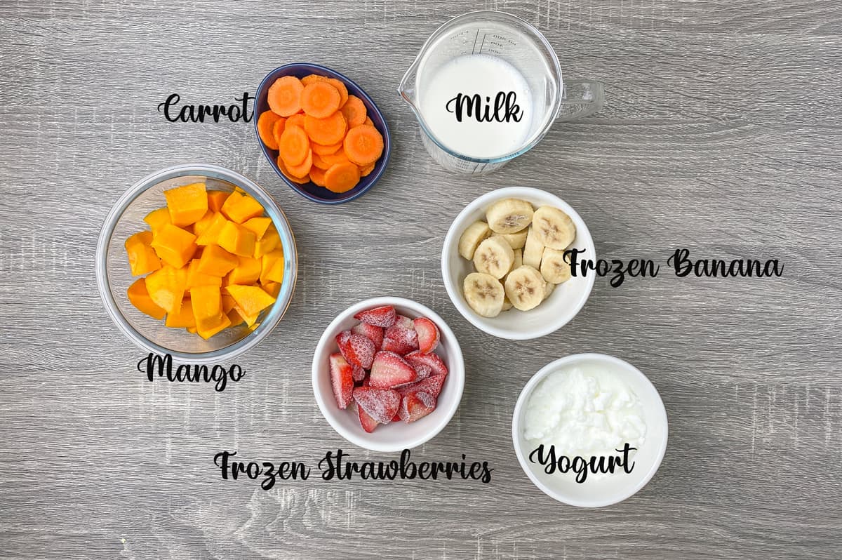 Ingredients for strawberry mango smoothie measured correctly in glass bowls and laid on gray table.