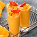 Close view of strawberry mango smoothie served in glasses, garnished with mango cubes and strawberry slices.