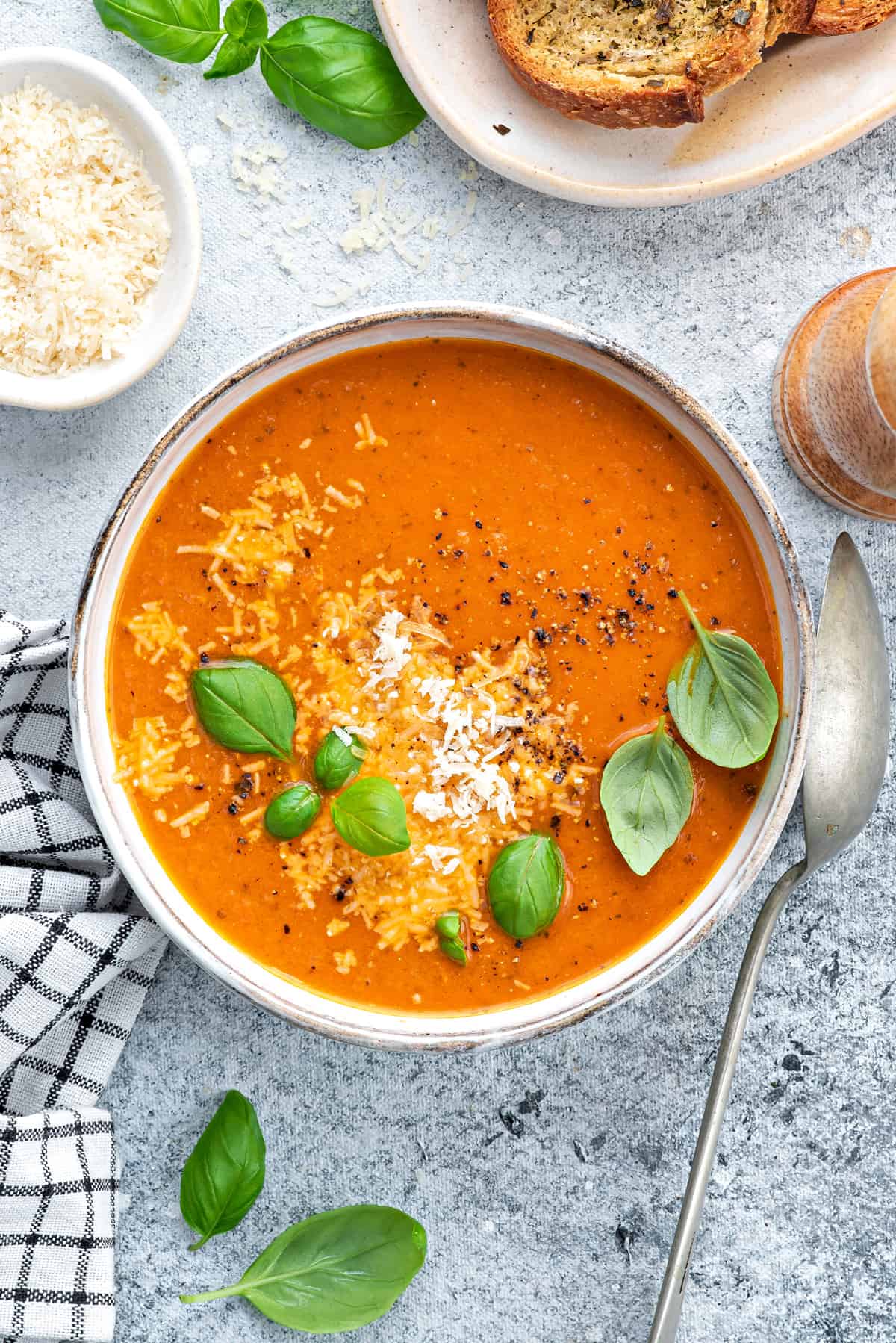 Bowl of tomato basil soup garnished with fresh basil and parmesan on a white table.
