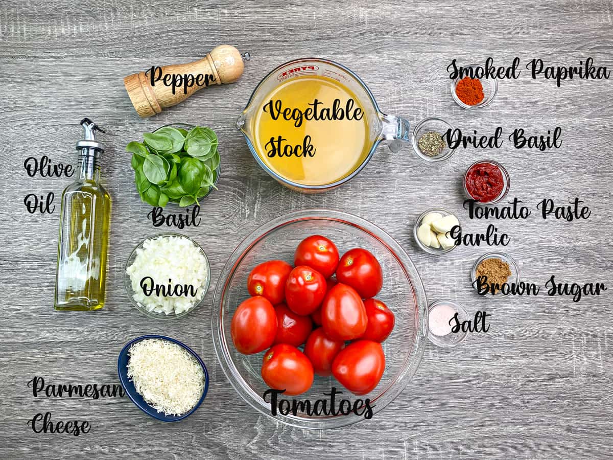 Ingredients for tomato and basil soup recipe measured in bowls and placed on a grey table.