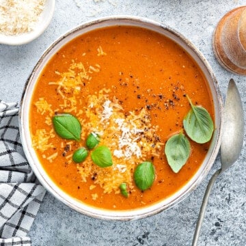 Bowl of tomato basil soup garnished with fresh basil and parmesan on a white table.