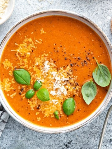 Bowl of tomato basil soup garnished with fresh basil and parmesan on a white table.