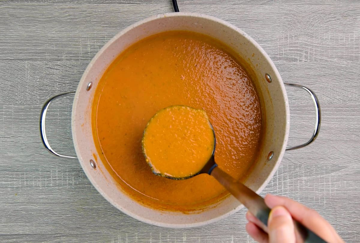 Ladleful of soup held above pot. Showing rich, creamy consistency.