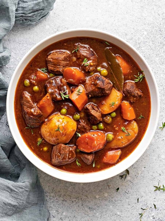 A white bowl of instant pot beef stew meat and gravy with potatoes, carrots and peas.