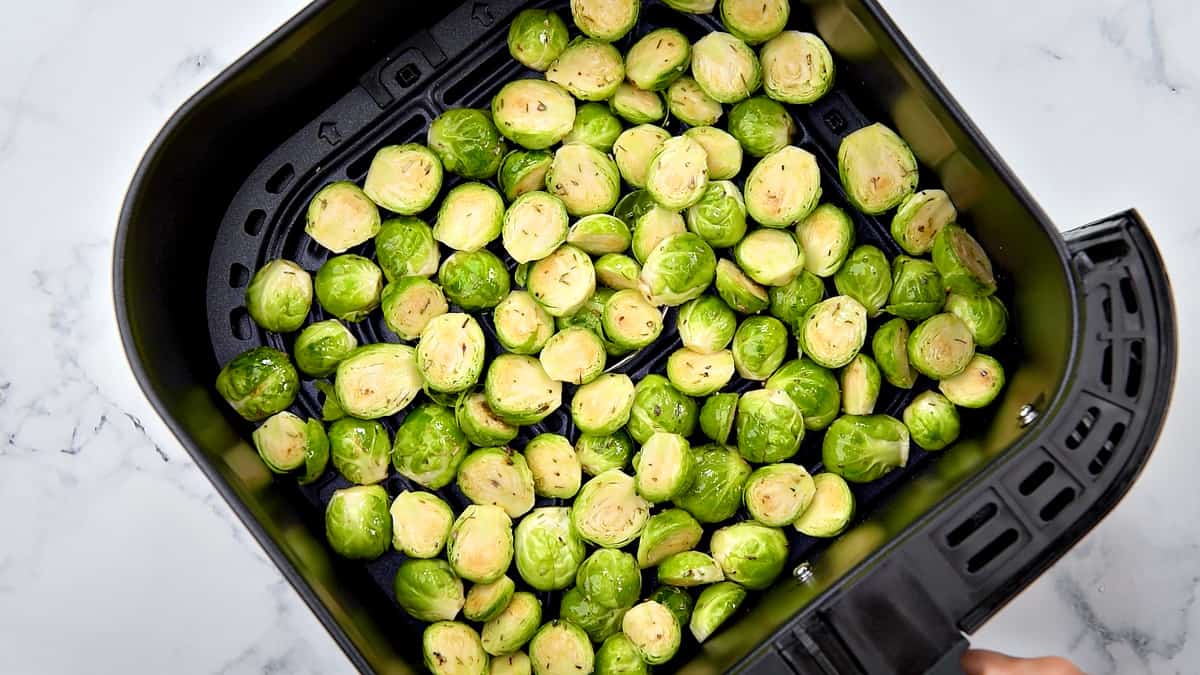 Raw halved sprouts in the air fryer basket.