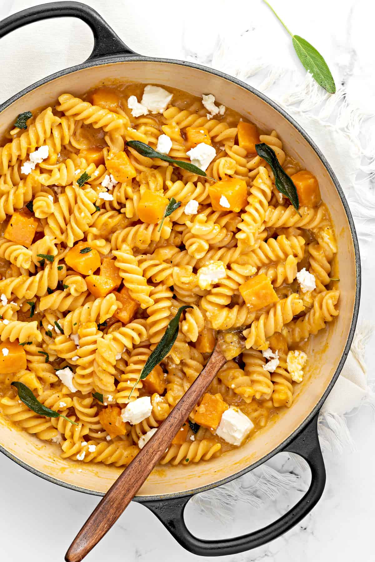 Squash pasta with feta cheese and crisp sage in the skillet with a wooden spoon.