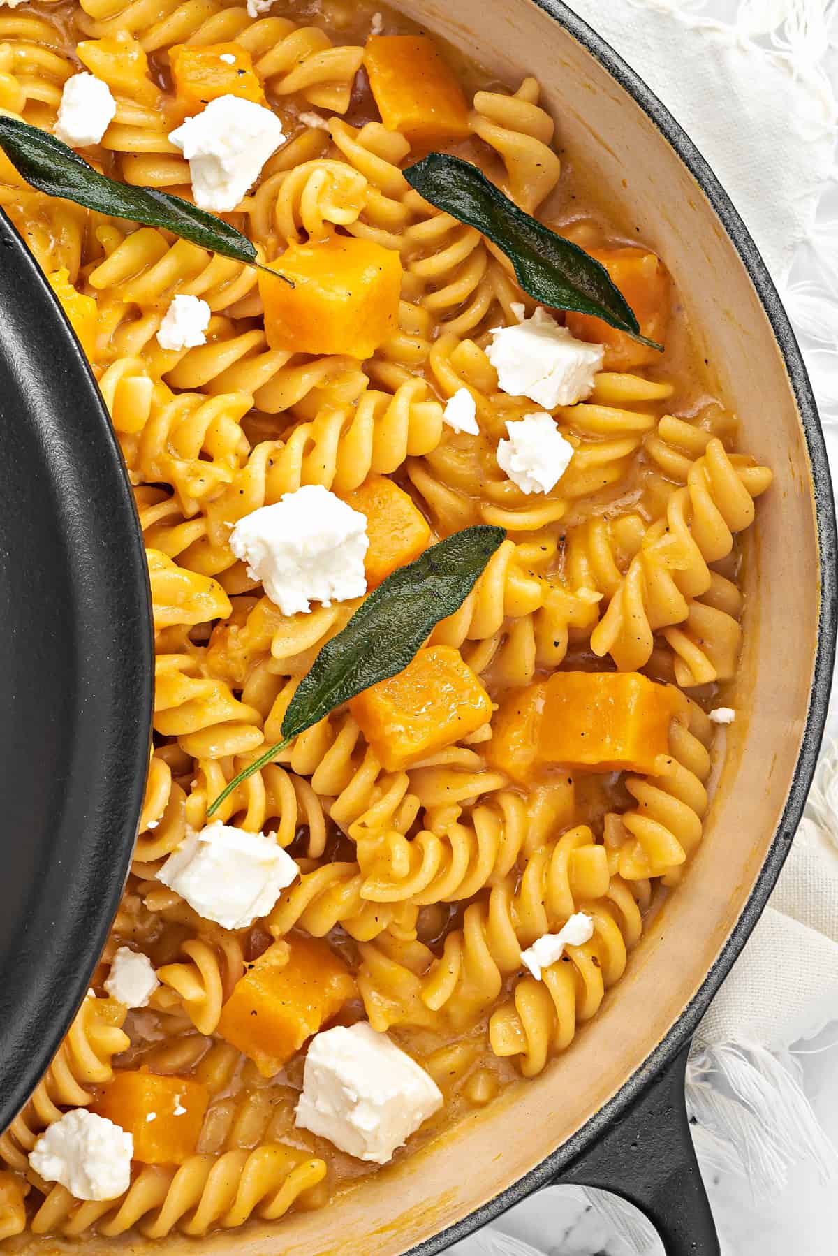 close up of healthy butternut squash pasta with crisp sage and feta cheese in pan.