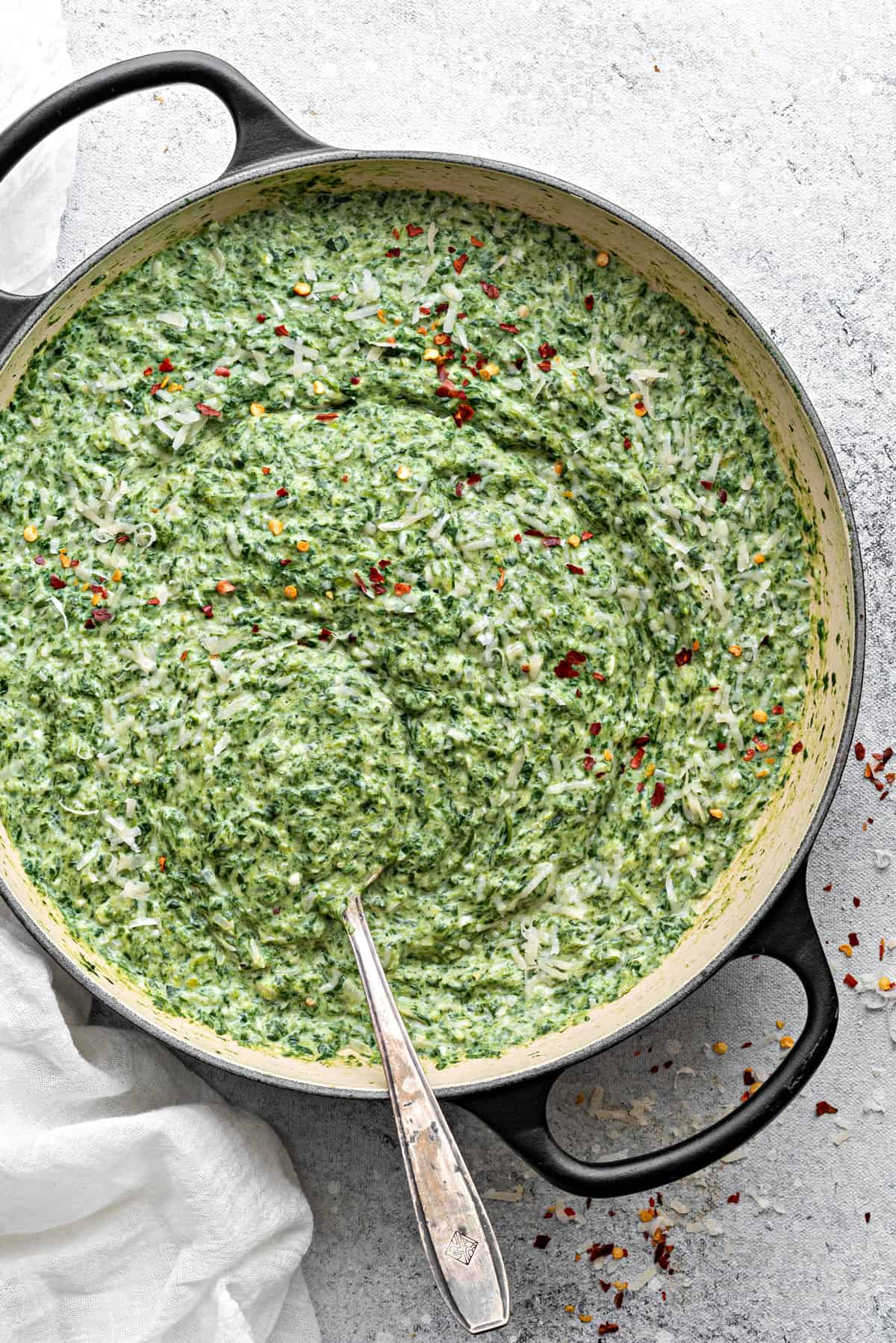 Homemade creamed spinach in a large cooking pot, with sprinkles of red pepper on top.