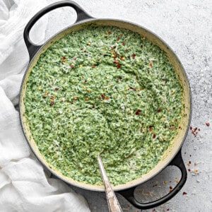 Homemade creamed spinach in a large cooking pot, with sprinkles of red pepper on top.