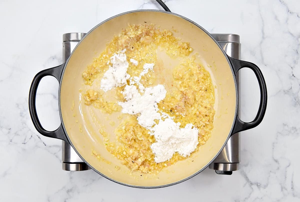 Adding flour to the cooking pot with sauteed garlic and onion.